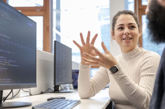 Eine Mitarbeiterin von Haavest sitzt mit einem Kollegen vor einem Monitor, während sie ihm etwas erklärt.