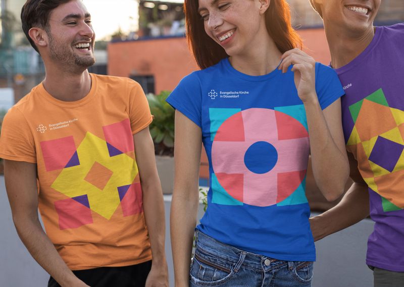 Fröhliche junge Menschen in bunten T-Shirts mit dem Keyvisual der Evangelischen Kirche in Düsseldorf.